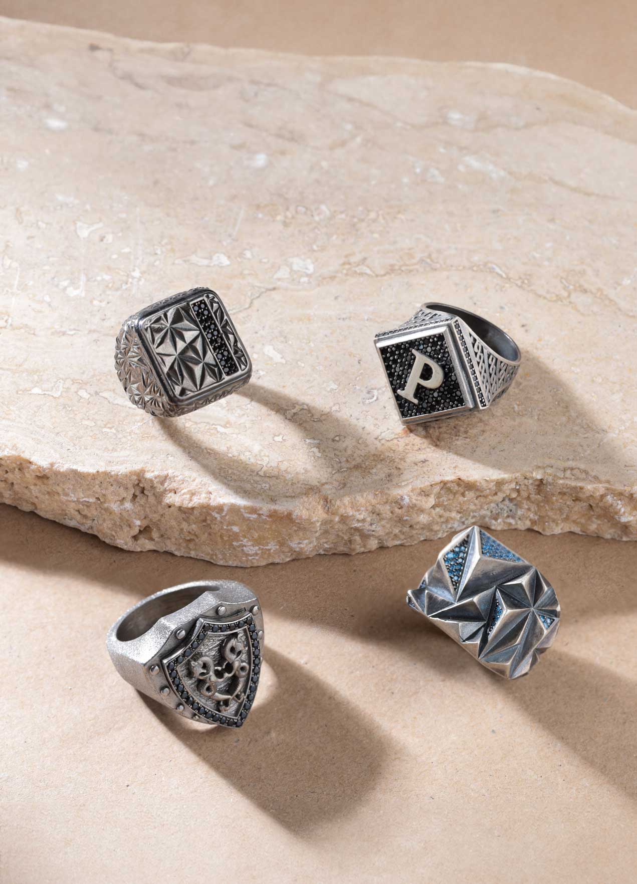 Variety of men’s rings including wedding bands, signet rings, statement rings, and gemstone designs in gold, platinum, titanium, and silver