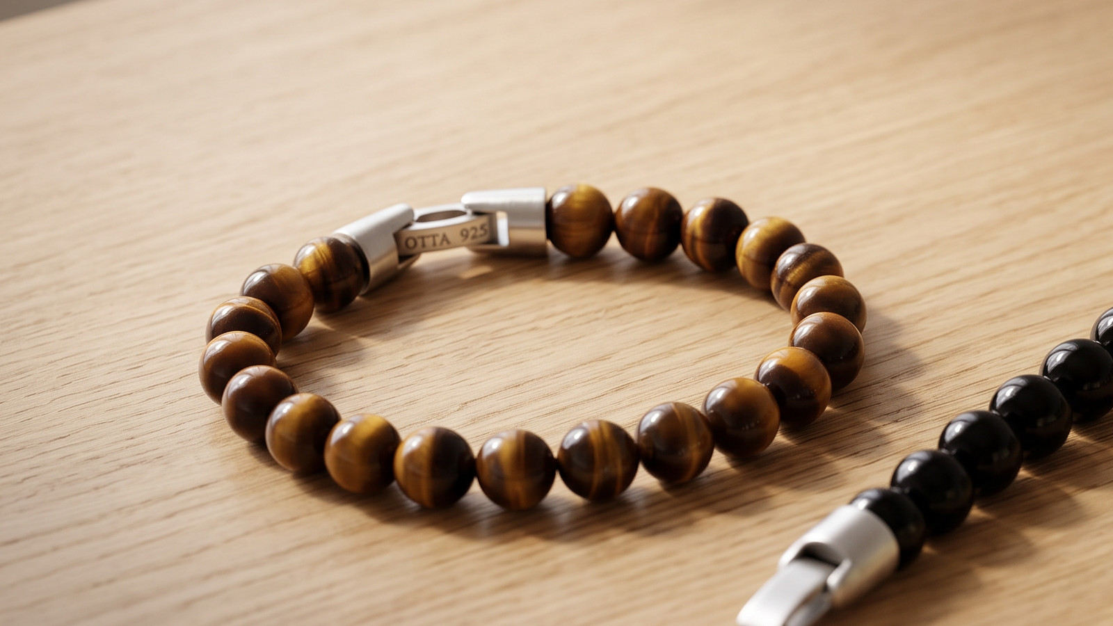 Tiger eye 8mm beaded bracelet with a silver OTTA 925 clasp next to an opened black onyx bead bracelet